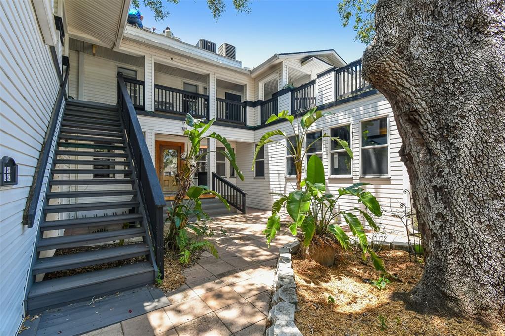 A two-story white building with a wooden staircase, balcony, and a paved courtyard with plants — 454 MAIN STREET, SAFETY HARBOR, FL