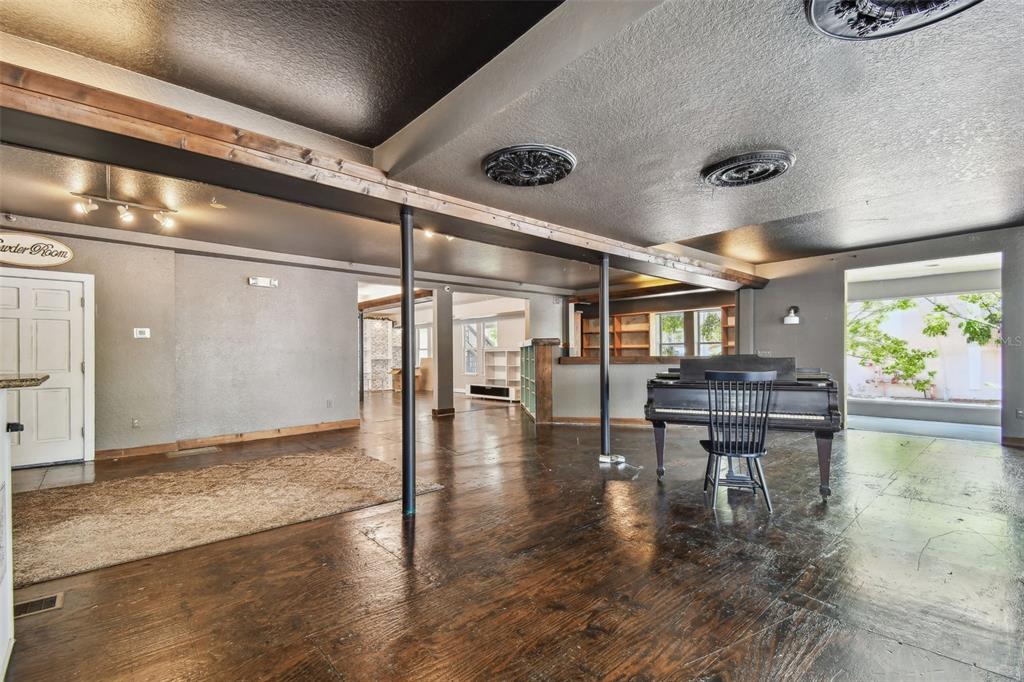 A large, open-concept room features dark wood floors, a grand piano, and exposed support poles — 454 MAIN STREET, SAFETY HARBOR, FL