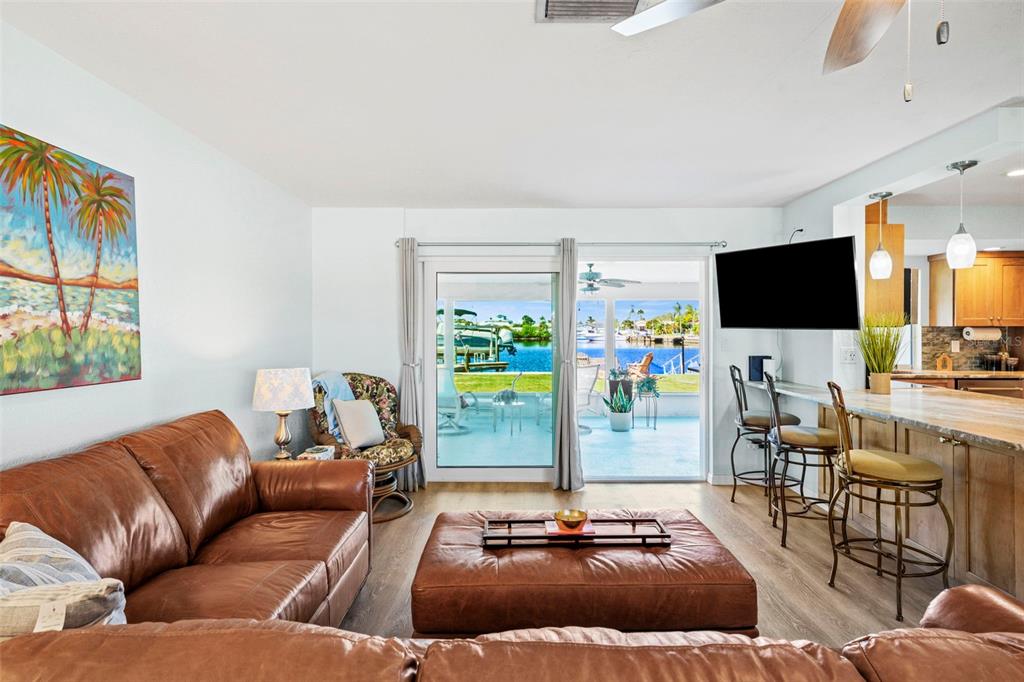 A living room with a leather sofa and ottoman overlooks a patio and waterfront view — 3711 FLORAMAR TERRACE, NEW PORT RICHEY, FL