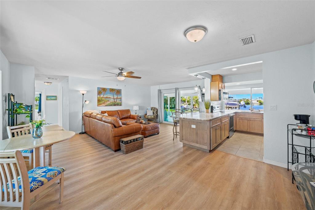 An open-concept living room and kitchen featuring wood-look flooring, a leather sofa, and water views — 3711 FLORAMAR TERRACE, NEW PORT RICHEY, FL