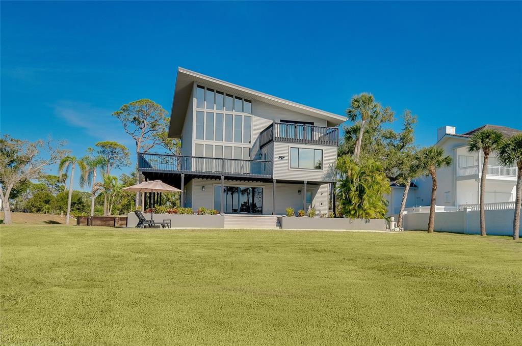 A two-story house with a slanted roof, large windows, and a deck overlooks a lawn — 1089 BAYSHORE DRIVE, ENGLEWOOD, FL