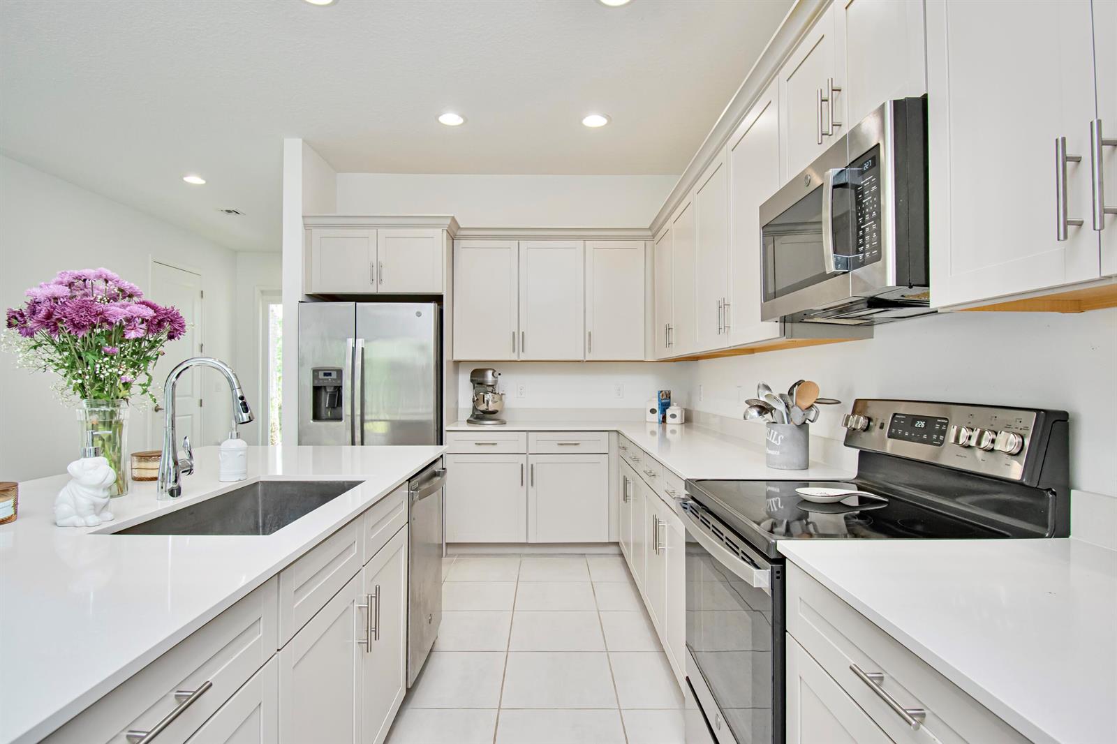 A kitchen features white cabinets, stainless steel appliances, quartz countertops, and a central island sink — 16420 Sandy Shore Drive, Loxahatchee FL 33470, LOXAHATCHEE, FL