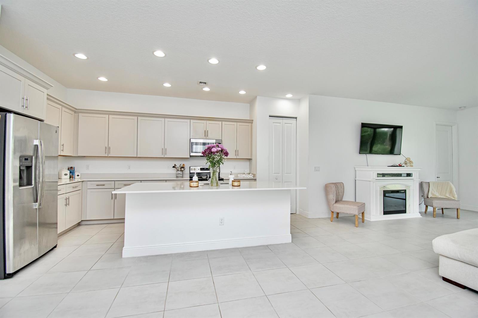 A modern kitchen with light-colored cabinets, a white island, and an adjacent fireplace area — 16420 Sandy Shore Drive, Loxahatchee FL 33470, LOXAHATCHEE, FL