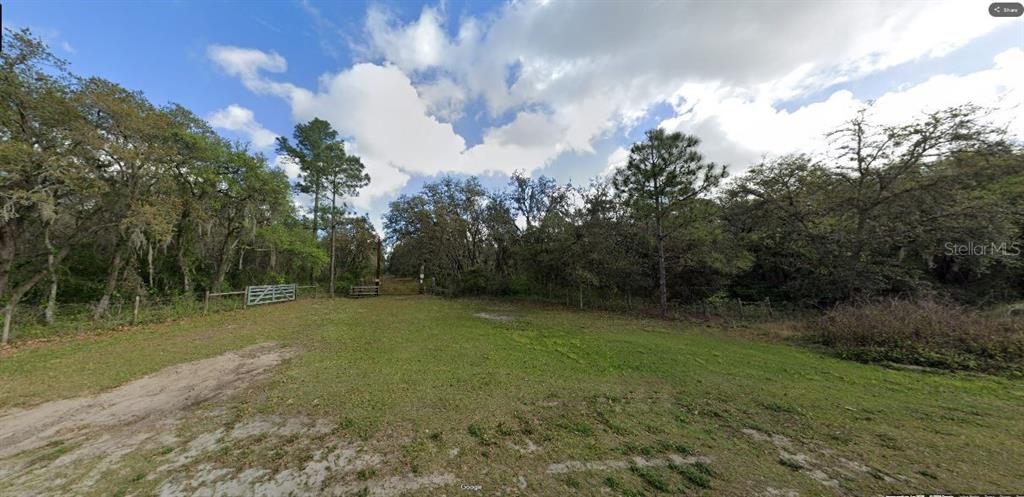 A grassy, open lot is bordered by dense trees and a wire fence with gates — DEEN STILL ROAD, POLK CITY, FL