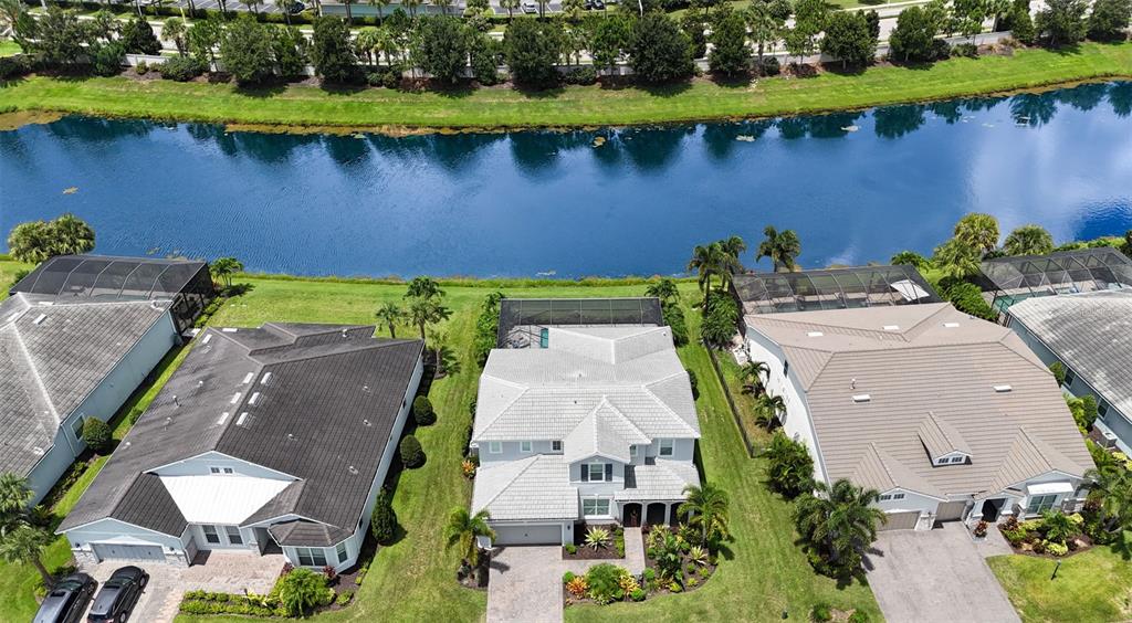 An aerial view shows three suburban houses with swimming pools along a narrow lake — 11810 BLUE HILL TRAIL, BRADENTON, FL