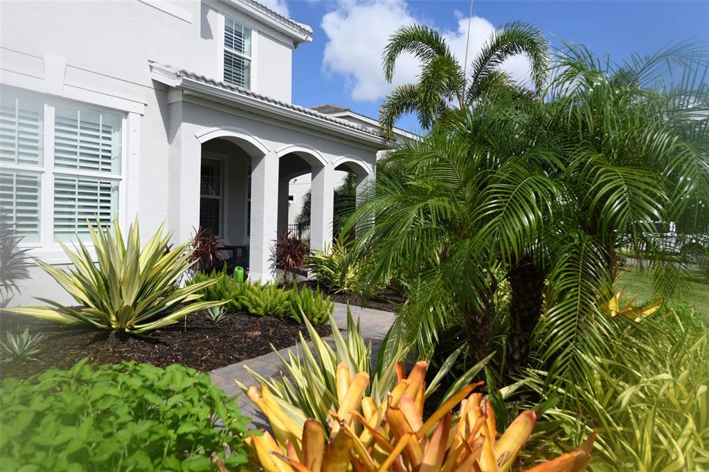 A white two-story house features a covered entryway with arched columns and lush tropical landscaping — 11810 BLUE HILL TRAIL, BRADENTON, FL