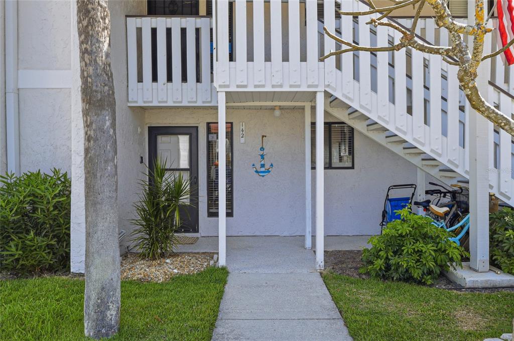 The exterior of a ground-floor apartment unit features a white staircase and an anchor decoration — 1801 GULF DRIVE N UNIT 142, BRADENTON BEACH, FL