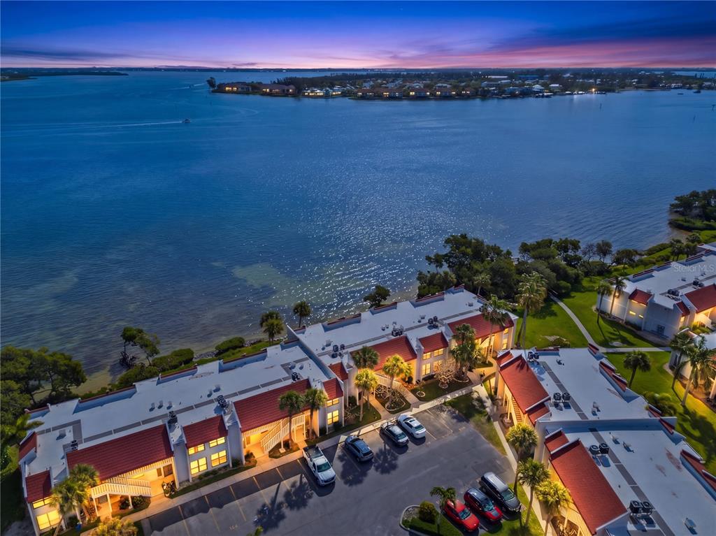An aerial view of a waterfront condominium complex with red-tiled roofs at dusk — 1801 GULF DRIVE N UNIT 142, BRADENTON BEACH, FL
