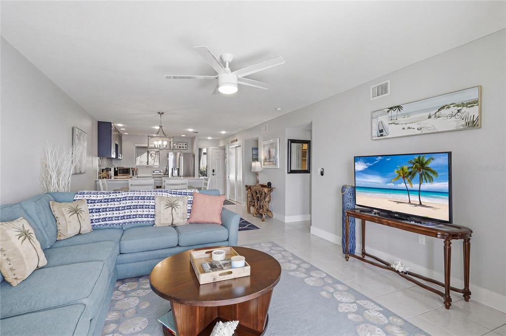 A living room features a blue sectional sofa, a round wooden coffee table, and a television — 1801 GULF DRIVE N UNIT 142, BRADENTON BEACH, FL