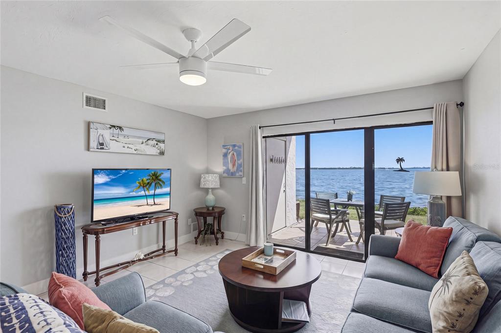 A living room features a ceiling fan, a television, and sliding doors overlooking the water — 1801 GULF DRIVE N UNIT 142, BRADENTON BEACH, FL