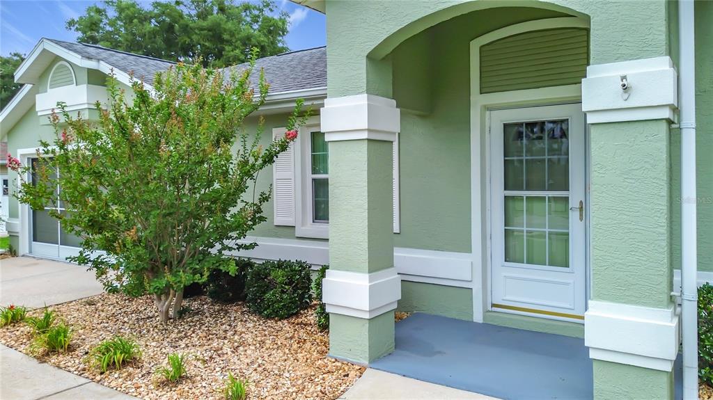 A light green house exterior features a covered entryway, white trim, and a small garden — 4771 NW 30TH PLACE, OCALA, FL