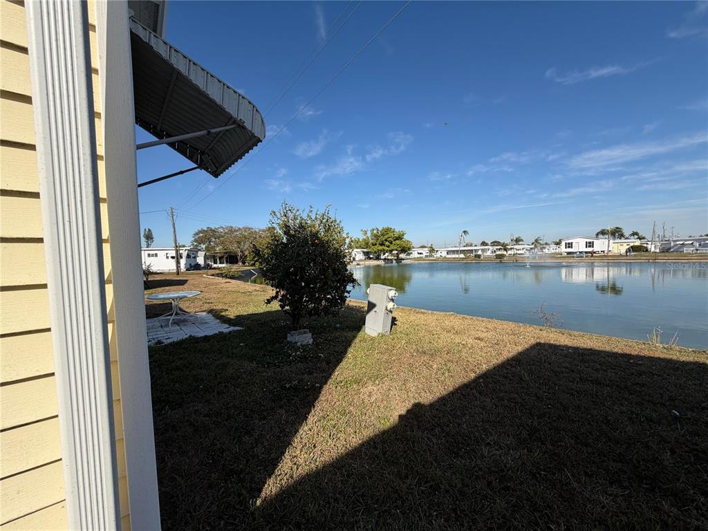 A view of a grassy backyard overlooking a pond with a fountain and neighboring homes — 5121 9TH STREET W, BRADENTON, FL