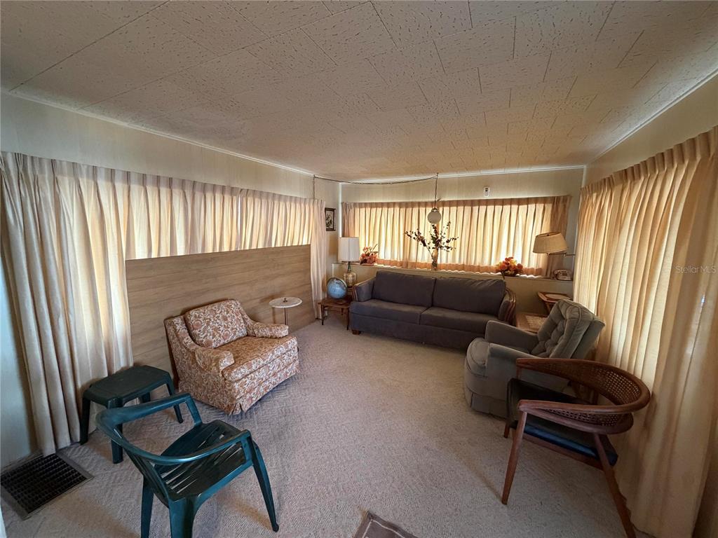 A living room features beige carpet, wood paneling, floor-to-ceiling curtains, and various seating options — 5121 9TH STREET W, BRADENTON, FL