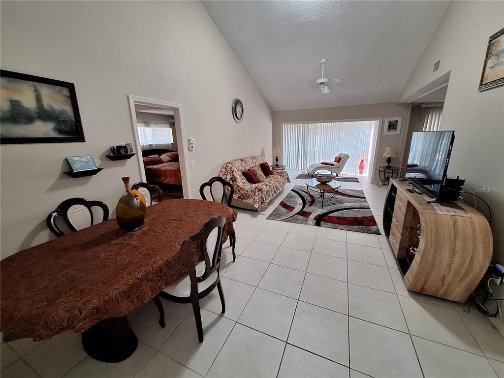An open-concept living and dining area features tile flooring, vaulted ceilings, and a sliding glass door — 1697 BROOKHOUSE CIRCLE UNIT 217, SARASOTA, FL