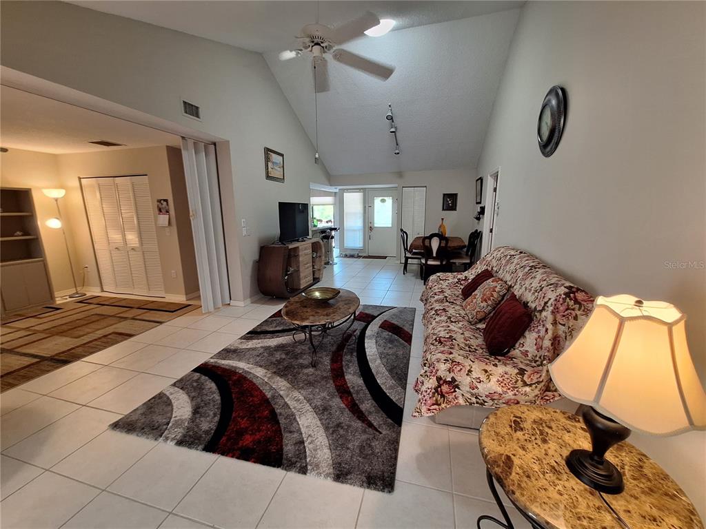A living room with tile floors, a vaulted ceiling, a ceiling fan, and a floral sofa — 1697 BROOKHOUSE CIRCLE UNIT 217, SARASOTA, FL