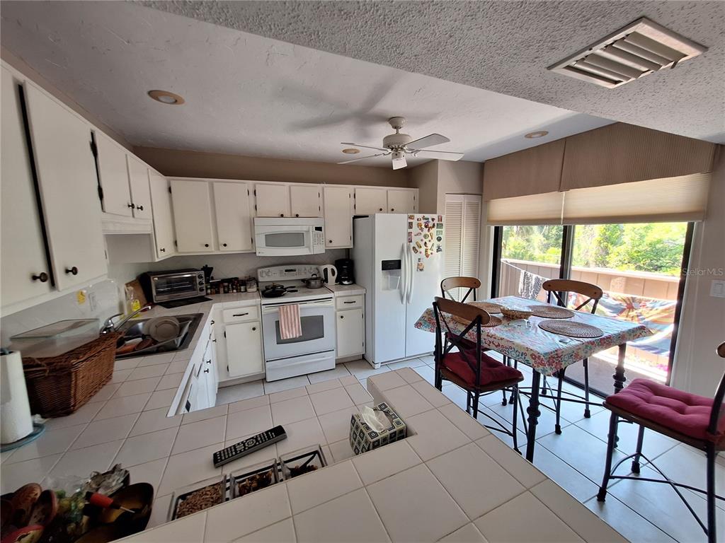 A kitchen features white cabinetry, tiled countertops, a white stove, and a dining area — 1697 BROOKHOUSE CIRCLE UNIT 217, SARASOTA, FL