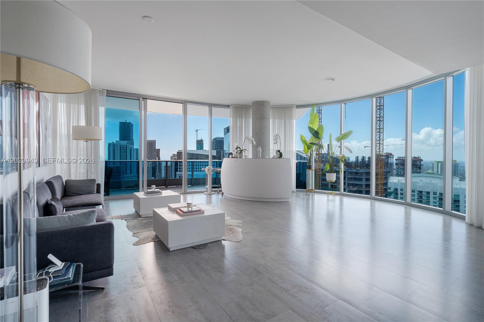 A modern living room features gray tile floors, floor-to-ceiling windows, and a curved white bar — 200 Biscayne Boulevard Way # 4902, Miami FL 33131, MIAMI, FL