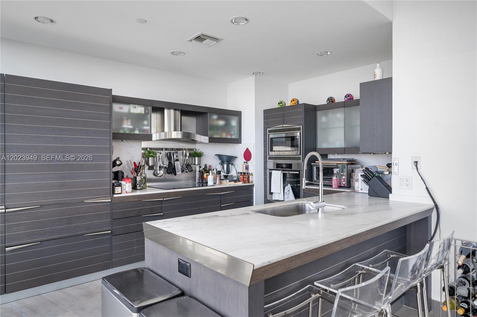 A modern kitchen features dark wood cabinetry, a marble-topped island, and stainless steel appliances — 200 Biscayne Boulevard Way # 4902, Miami FL 33131, MIAMI, FL