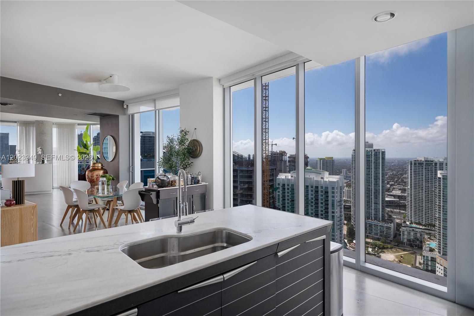 A modern kitchen island with a sink overlooks a dining area and city skyline views — 200 Biscayne Boulevard Way # 4902, Miami FL 33131, MIAMI, FL