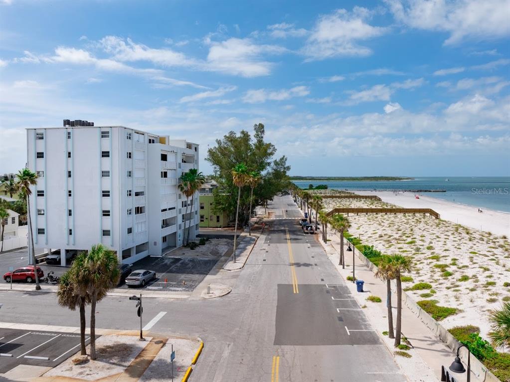 An aerial view shows a white multi-story building next to a road and sandy beach — 403 GULF WAY UNIT 601, ST PETE BEACH, FL