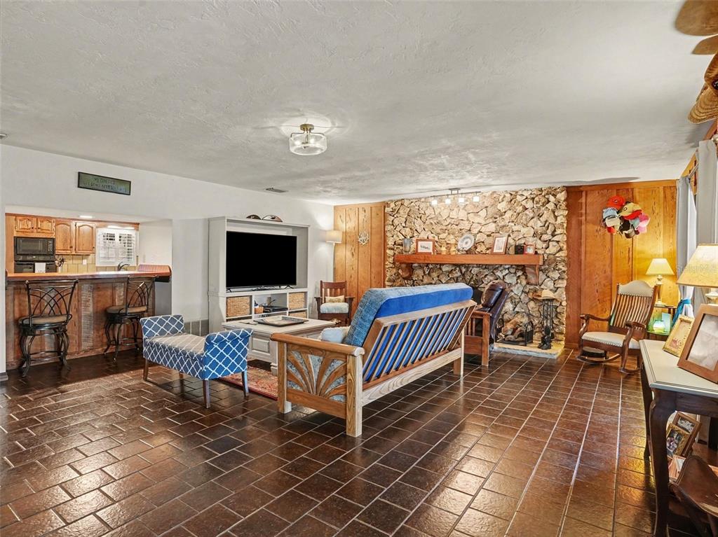 A living room with a stone fireplace, wood paneling, and dark tile flooring — 1390 E OHIO AVENUE, LAKE HELEN, FL