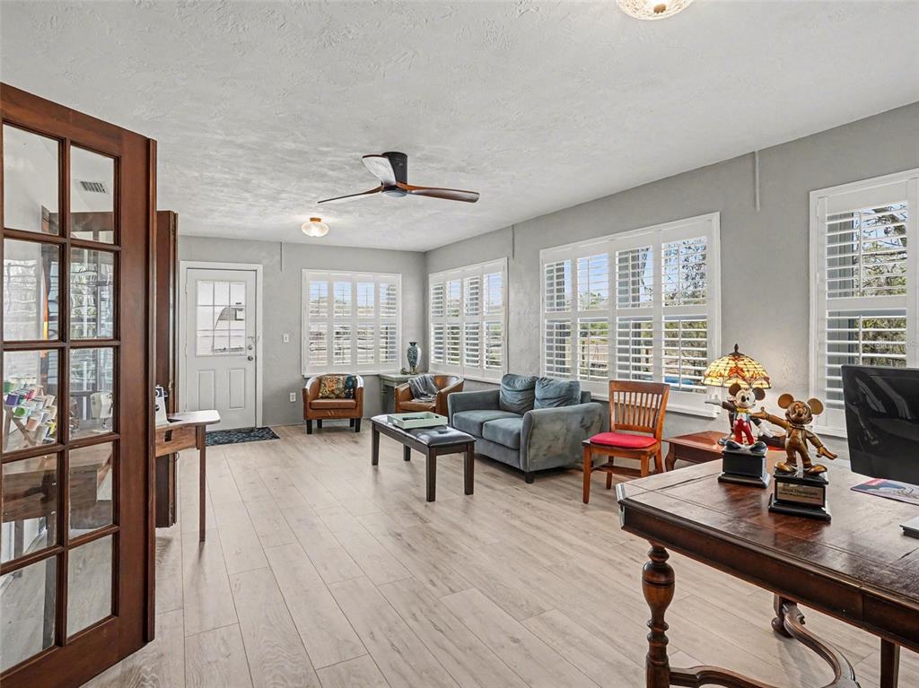 A living room with light wood-look flooring, a ceiling fan, and multiple windows with shutters — 1390 E OHIO AVENUE, LAKE HELEN, FL