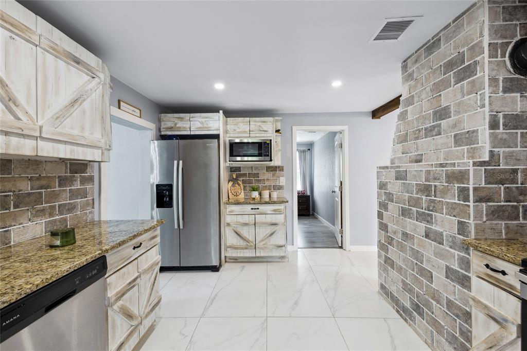 A kitchen features white farmhouse-style cabinets, granite countertops, brick accents, and light-colored tile flooring — 1845 SW HALTIWANGER ROAD, LAKE CITY, FL