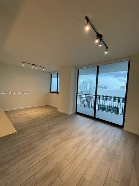 An empty living room features light wood-look tile flooring, track lighting, and a balcony view — 999 SW 1st Ave # 3115, Miami FL 33130, MIAMI, FL