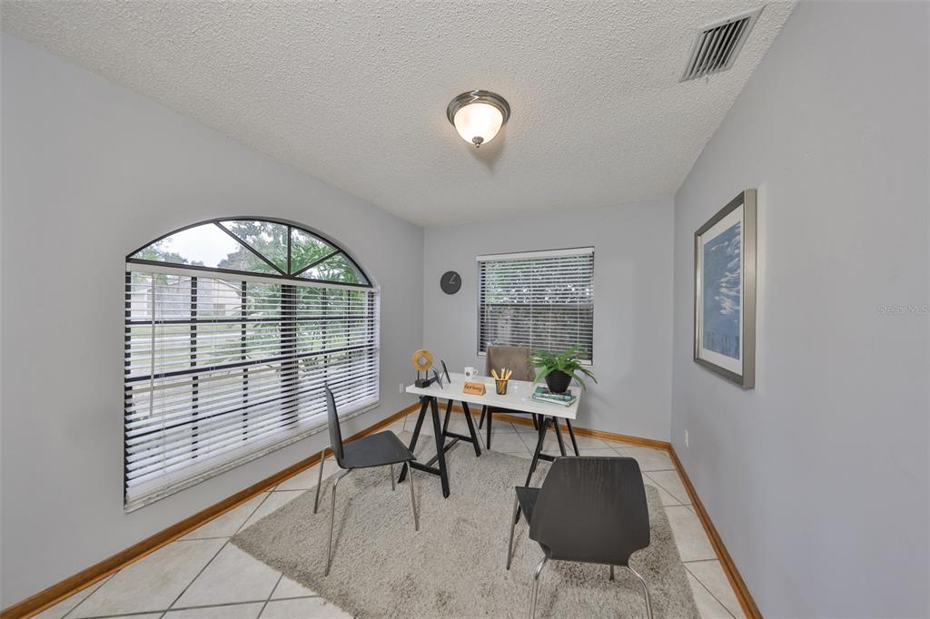 A home office features a white desk, two chairs, a rug, and an arched window — 3818 BISCAY PLACE, LAND O LAKES, FL
