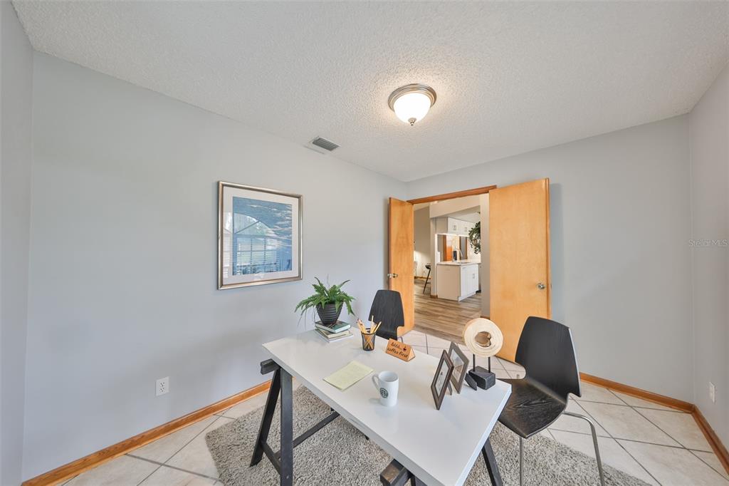 A home office with a white desk, two black chairs, and double doors leading inside — 3818 BISCAY PLACE, LAND O LAKES, FL