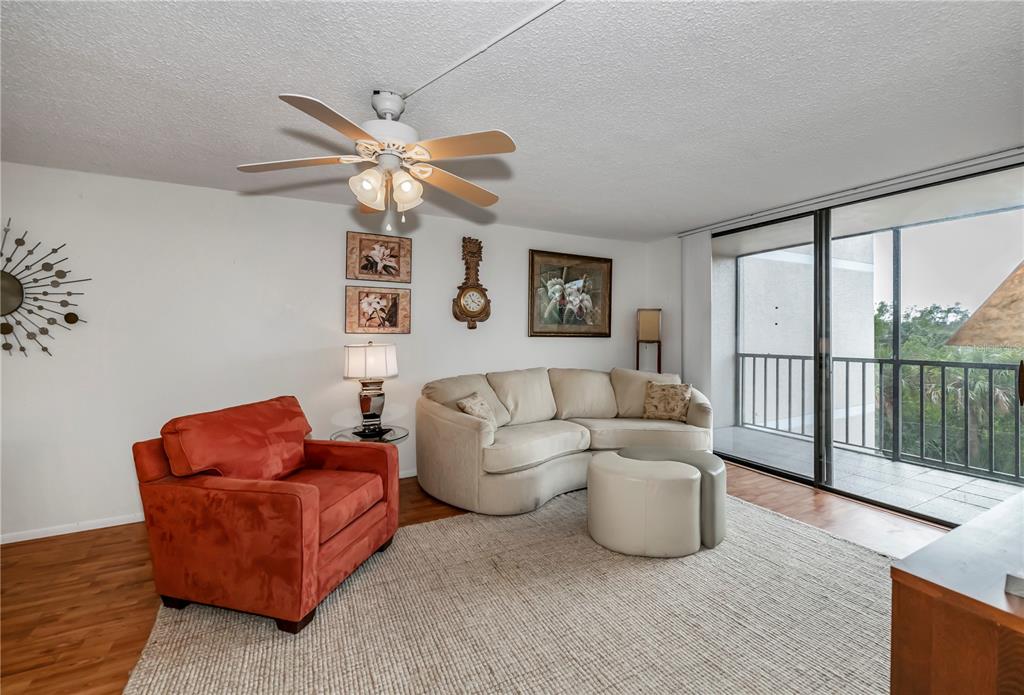 A living room features a curved beige sofa, an orange armchair, and a balcony view — 25188 MARION AVENUE UNIT D205, PUNTA GORDA, FL