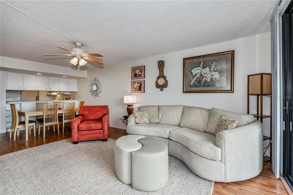 A living room with a curved sofa, red armchair, dining area, and light wood flooring — 25188 MARION AVENUE UNIT D205, PUNTA GORDA, FL