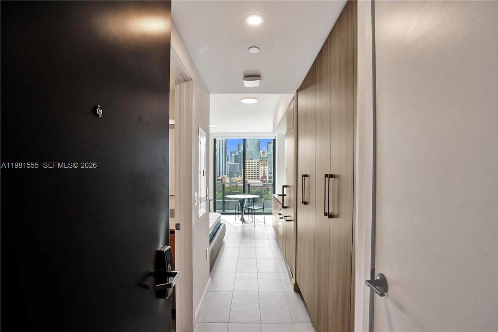 A view from an entryway looking down a tiled hallway toward a city skyline window — 121 NE 5 St # 801B, Miami FL 33132, MIAMI, FL