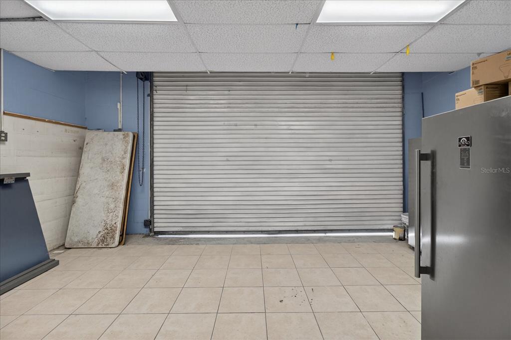A room with tiled flooring, a large roll-up metal door, and a drop ceiling — 2024 GRANT STREET, TAMPA, FL