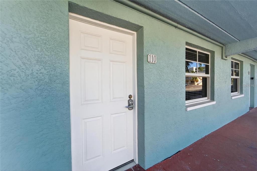 An exterior view of a ground-level apartment unit with a white door and window — 19417 GULF BOULEVARD UNIT F110, INDIAN ROCKS BEACH, FL
