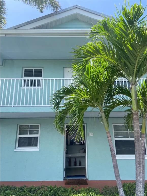 A light blue two-story building exterior features a white front door and palm trees — 19417 GULF BOULEVARD UNIT F110, INDIAN ROCKS BEACH, FL