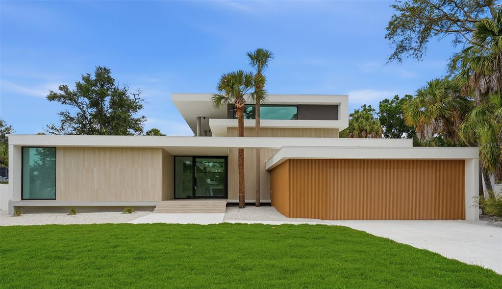 A modern two-story house features a flat roof, light stone siding, and a slatted garage door — 359 N SHORE DRIVE, SARASOTA, FL