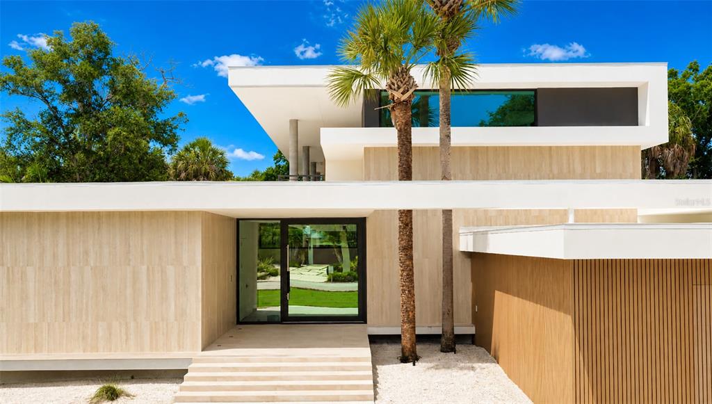A modern house exterior features a stone facade, a glass front door, and palm trees — 359 N SHORE DRIVE, SARASOTA, FL