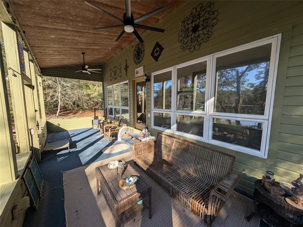 A covered porch with wicker furniture, ceiling fans, and large windows overlooking a wooded area — 14730 SE 61ST STREET ROAD, OCKLAWAHA, FL