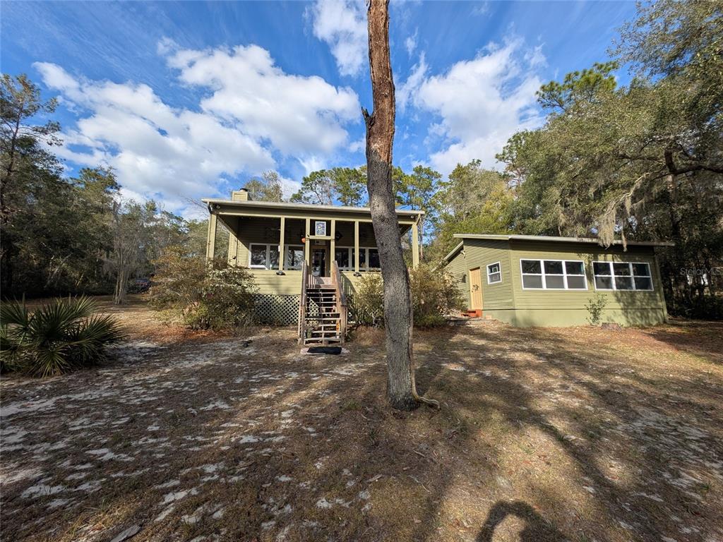 A green house with a raised porch and stairs stands in a wooded, sandy yard — 14730 SE 61ST STREET ROAD, OCKLAWAHA, FL
