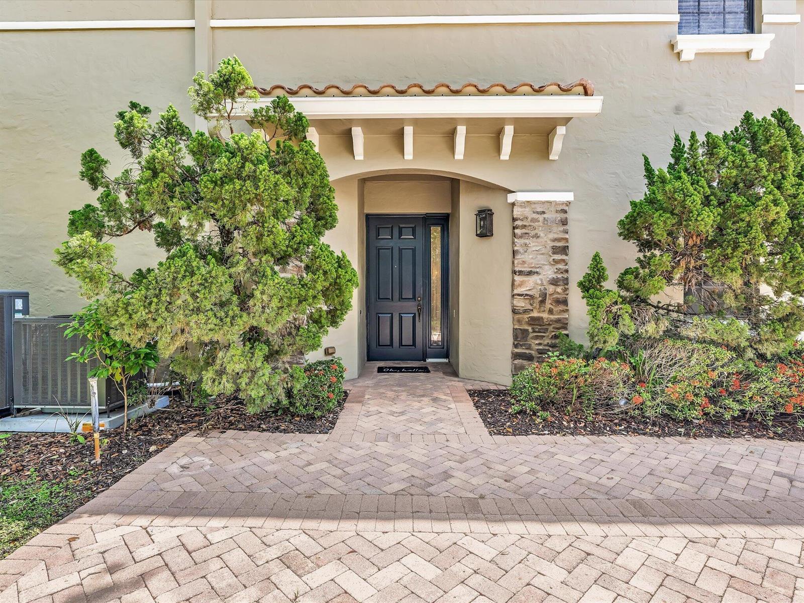 A front entryway with a dark door, stone pillar, and brick walkway surrounded by landscaping — 7531 Old Thyme Court, Parkland FL 33076, PARKLAND, FL
