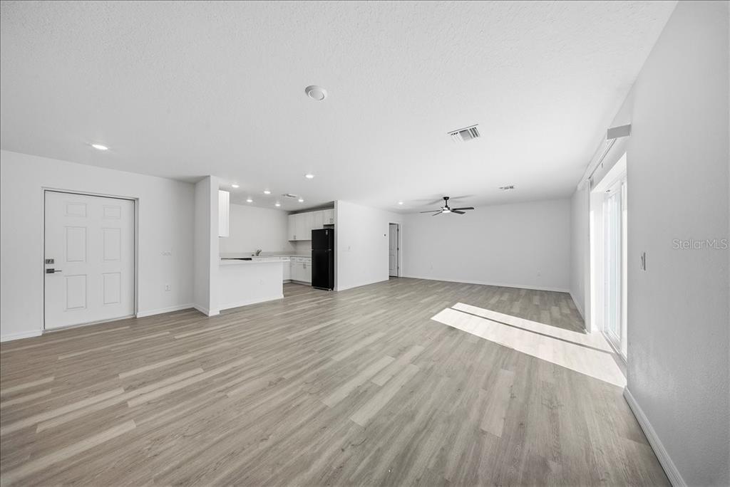An open-concept living area features light wood-look flooring, white walls, and a kitchen with black appliances — 5565 LAVENDER AVENUE, NORTH PORT, FL
