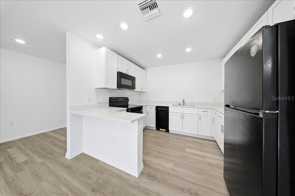 A kitchen features white cabinets, black appliances, light wood-look flooring, and a peninsula counter — 5565 LAVENDER AVENUE, NORTH PORT, FL