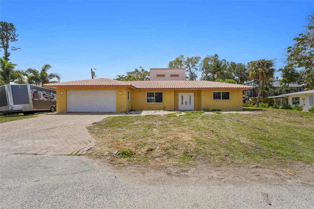 A yellow single-story house with a tile roof, a two-car garage, and a paved driveway — 1613 IDLE LANE, SARASOTA, FL