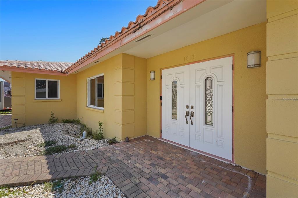 The exterior of a yellow house features a brick walkway leading to white double doors — 1613 IDLE LANE, SARASOTA, FL