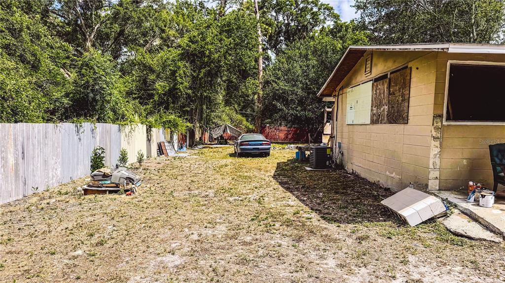 A side view of a house with a fenced yard, a parked car, and debris — 6722 SW 53RD AVENUE, GAINESVILLE, FL