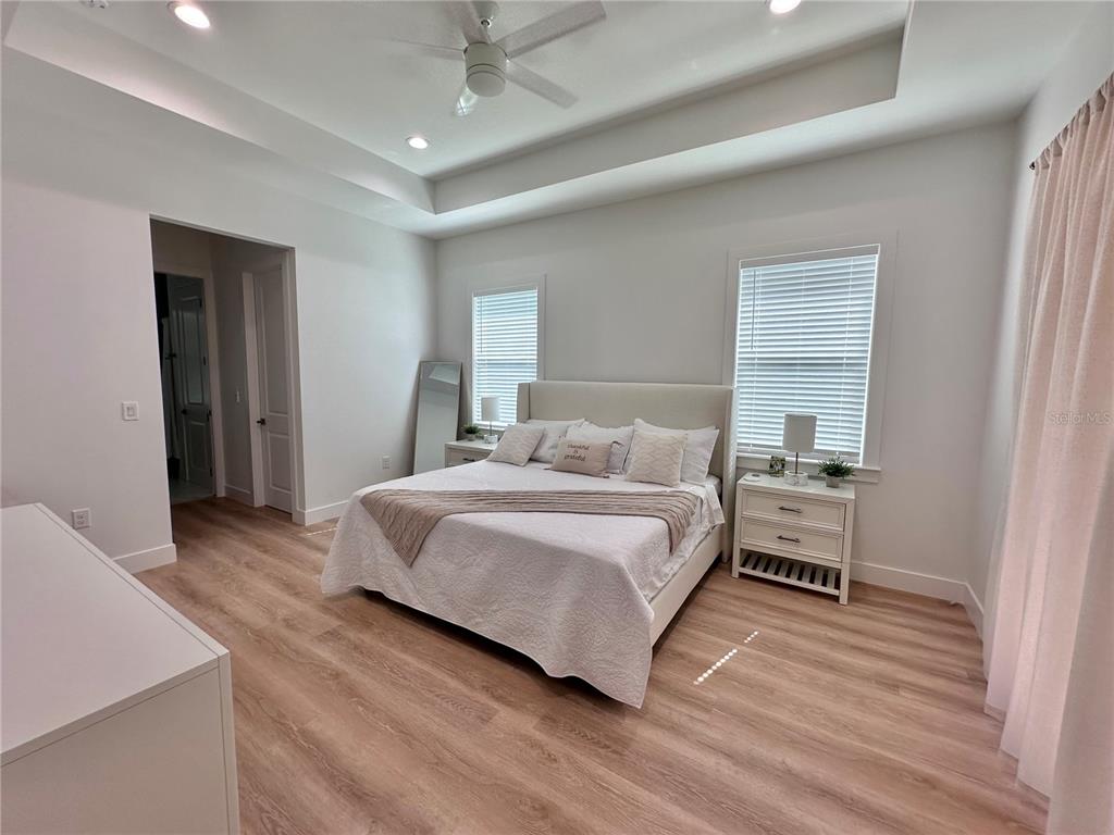 A bedroom features light wood-look flooring, white walls, a tray ceiling, and a king-sized bed — 4625 RHAPSODY AVENUE, NORTH PORT, FL