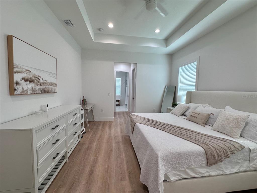 A bedroom features a tray ceiling, light wood flooring, a white dresser, and a bed — 4625 RHAPSODY AVENUE, NORTH PORT, FL