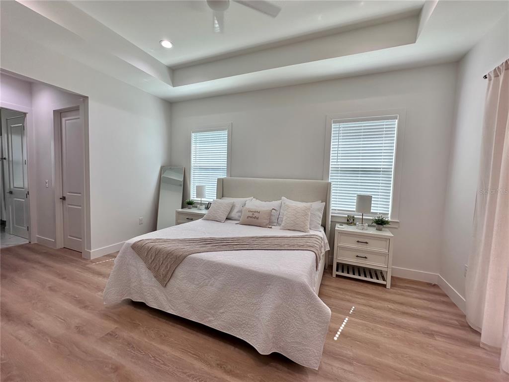 A bedroom features light wood-look flooring, a tray ceiling, and a bed centered between windows — 4625 RHAPSODY AVENUE, NORTH PORT, FL