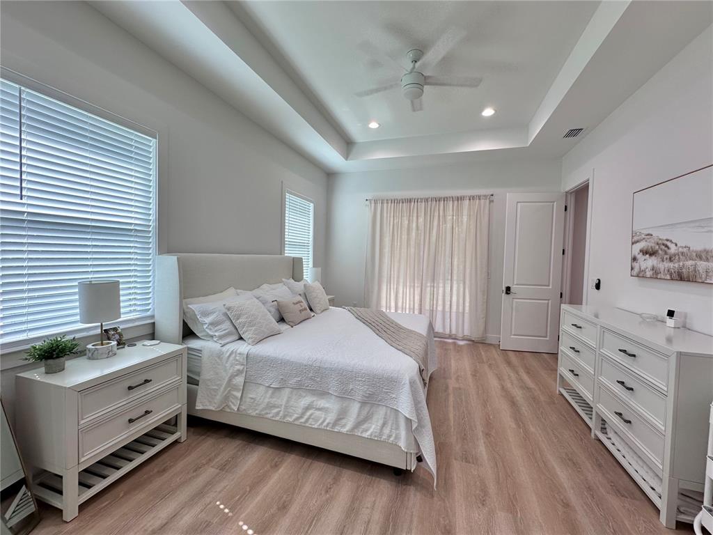 A bedroom features a king bed, white furniture, light wood flooring, and a tray ceiling — 4625 RHAPSODY AVENUE, NORTH PORT, FL